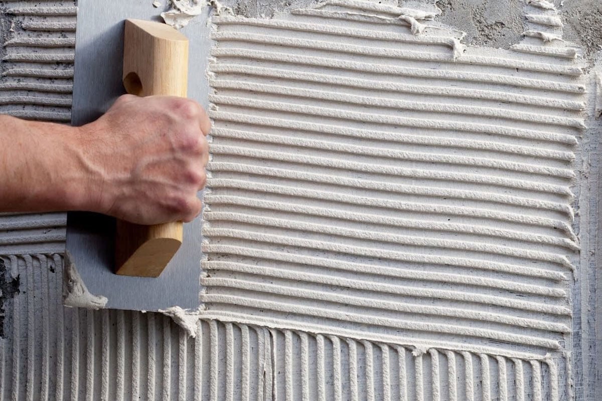 man applying masonry scratch coat to cinder block outdoor kitchen