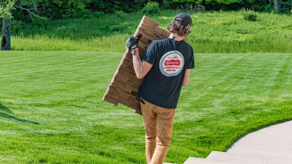 Installer carrying an RTA outdoor kitchen panel across a backyard